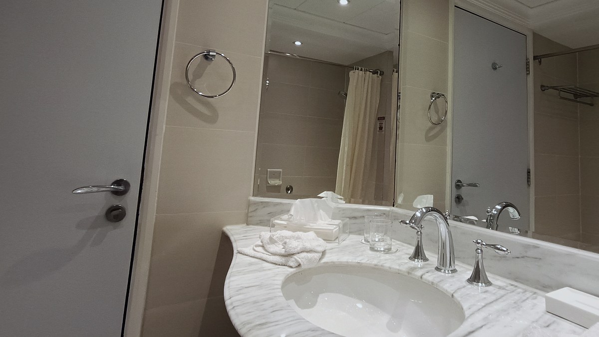 Baño de una habitación de hotel con encimera de mármol, grifería y espejos en los que se refleja la cortina de la ducha
