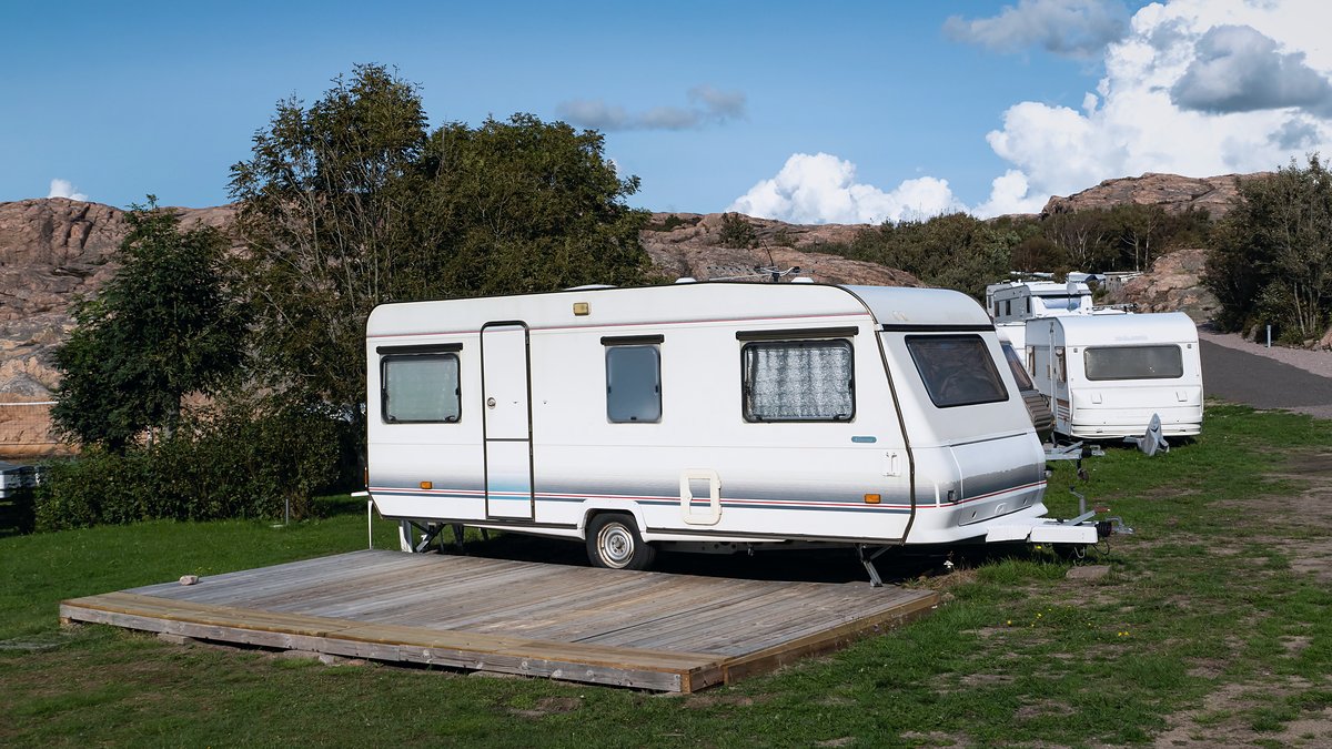 Caravanas blancas aparcadas en las parcelas de césped de un camping junto a árboles y rocas