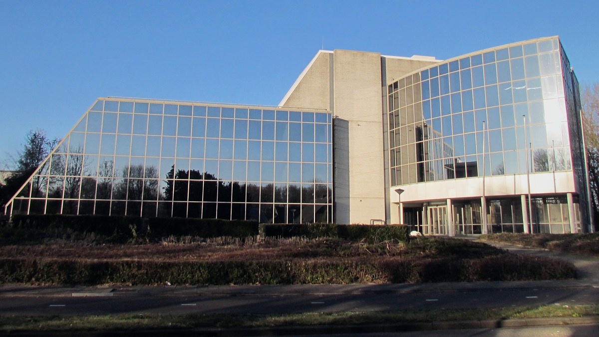 Edificio de oficinas con fachada de cristal espejado y un cuerpo central de ladrillo claro bajo un cielo azul