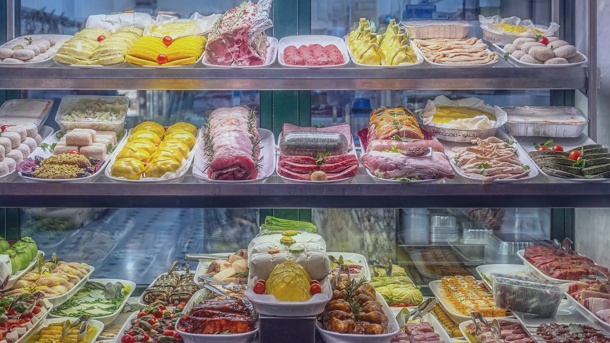 Vitrina refrigerada de una charcutería con bandejas de embutidos, quesos y platos preparados